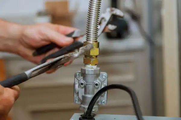 Hands skillfully using pliers to tighten a metal hose during a meticulous gas line installation, while a wrench holds the gas valve steady.