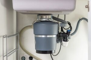 A garbage disposal unit attached under a kitchen sink, with various hoses and pipes connected.