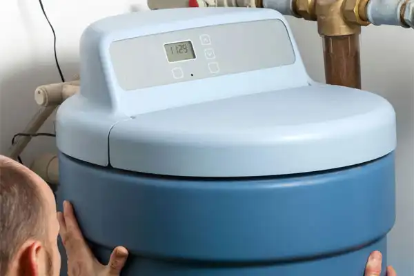 A person is fine-tuning a blue water softener tank equipped with a digital control panel, showing expertise in water softener installation.