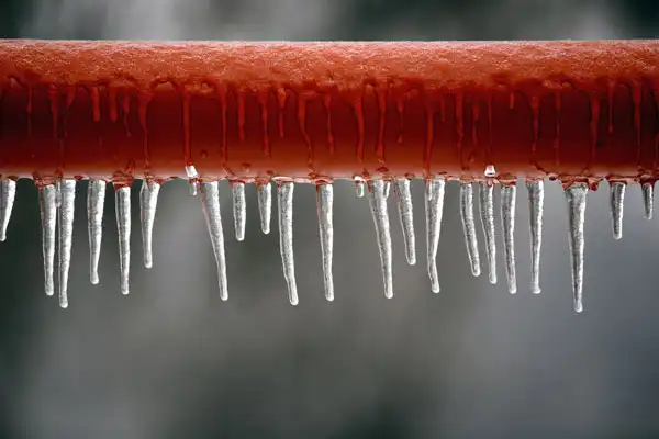 A red pipe, glistening with icicles, hints at a chilly tale of burst pipe repair, set against a blurred gray background.
