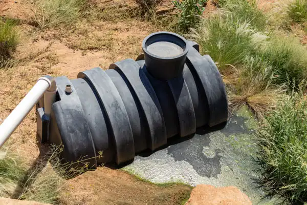 A black plastic septic tank partially buried in the ground, surrounded by grass and dirt, with a pipe connected to it, stands ready for septic tank repair to ensure everything flows smoothly.