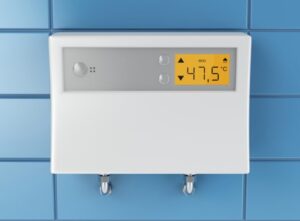 Digital thermostat on a blue tiled wall showing a temperature of 47.5°C with eco mode symbol and two control buttons below.