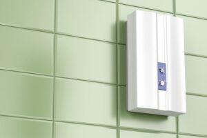 A white wall-mounted device with control dials is installed on a green tiled wall.